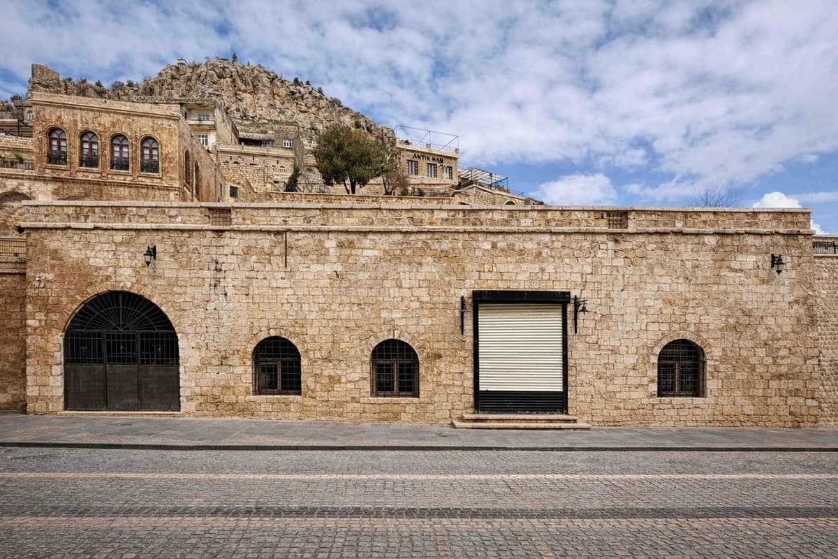 Kervansaray — Mardin'in tarihi taş yapısı, kemerli cephesi ve arkada kale yamacı